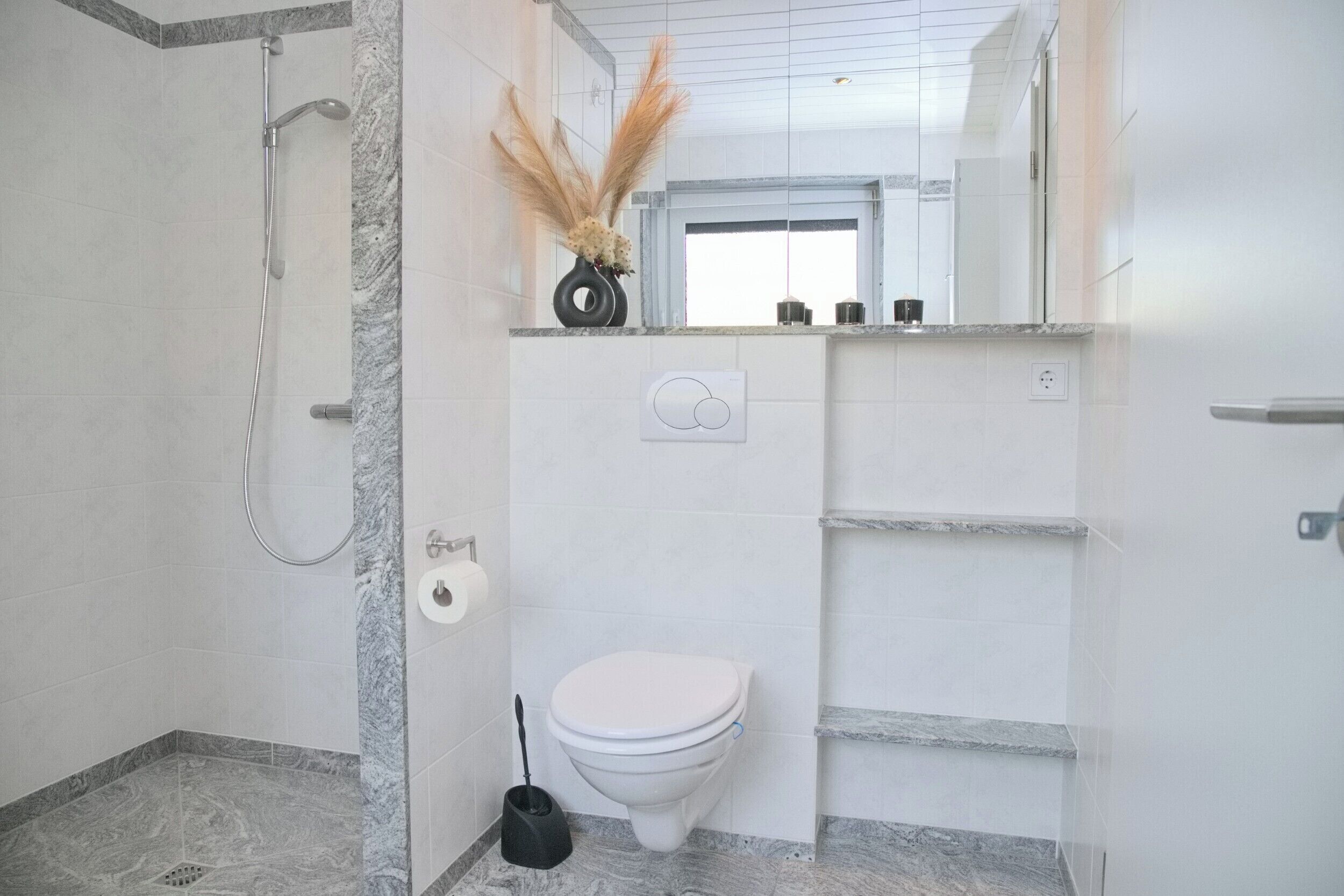 A modern bathroom with a shower, toilet, and marble flooring.