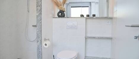 A modern bathroom with a shower, toilet, and marble flooring.