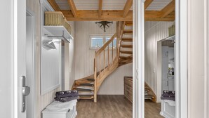 En trappe med trægelændere fører op til en anden etage, en hvid dør med metalgreb og en kurv på væggen.