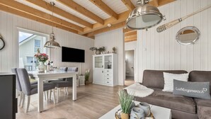 En moderne stue med træloft, en lædersofa i brunt, et hvidt spisebord og et fjernsyn monteret på væggen.