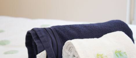 A neatly folded navy blue towel and a white towel with two bottles of Revitalizing Shampoo & Conditioner on a bed with a white sheet and green leaf patterns.