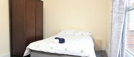 A bedroom with a bed, a wardrobe, and a window with curtains.