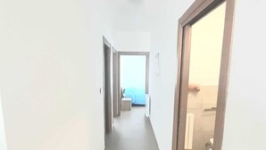 Un couloir étroit avec une porte donnant sur une pièce où se trouvent un lit et une table de chevet.