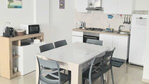 Une cuisine compacte comprenant un coin repas, des meubles blancs, une cuisinière à gaz et un petit réfrigérateur.