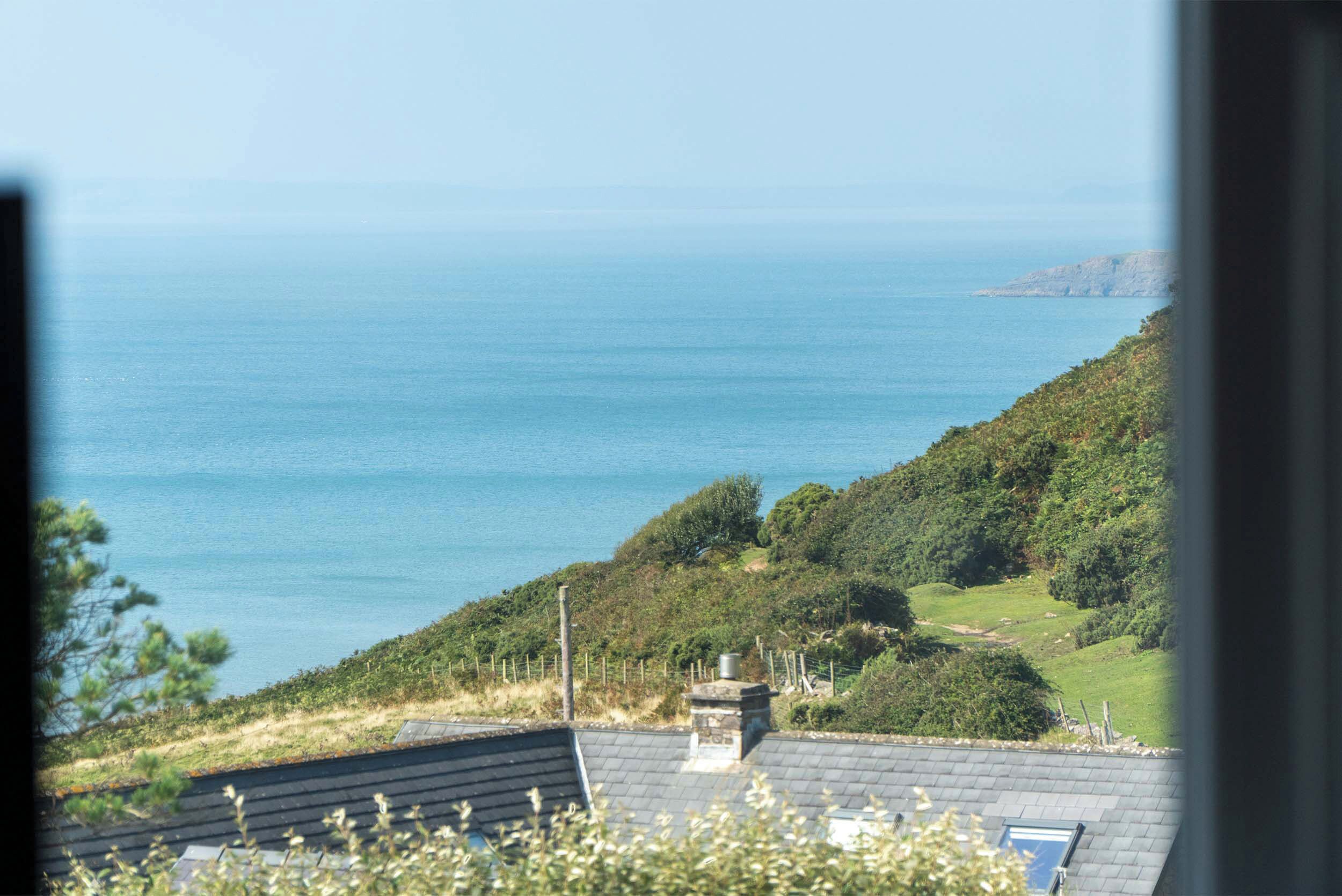 A coastal view with a house on a hill overlooking the sea.