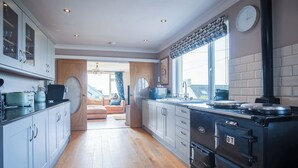 A modern kitchen with a large stove, cabinets, and a view to the living area. - Carissima - 4 Bedroom House - Rhossili (Swansea)
