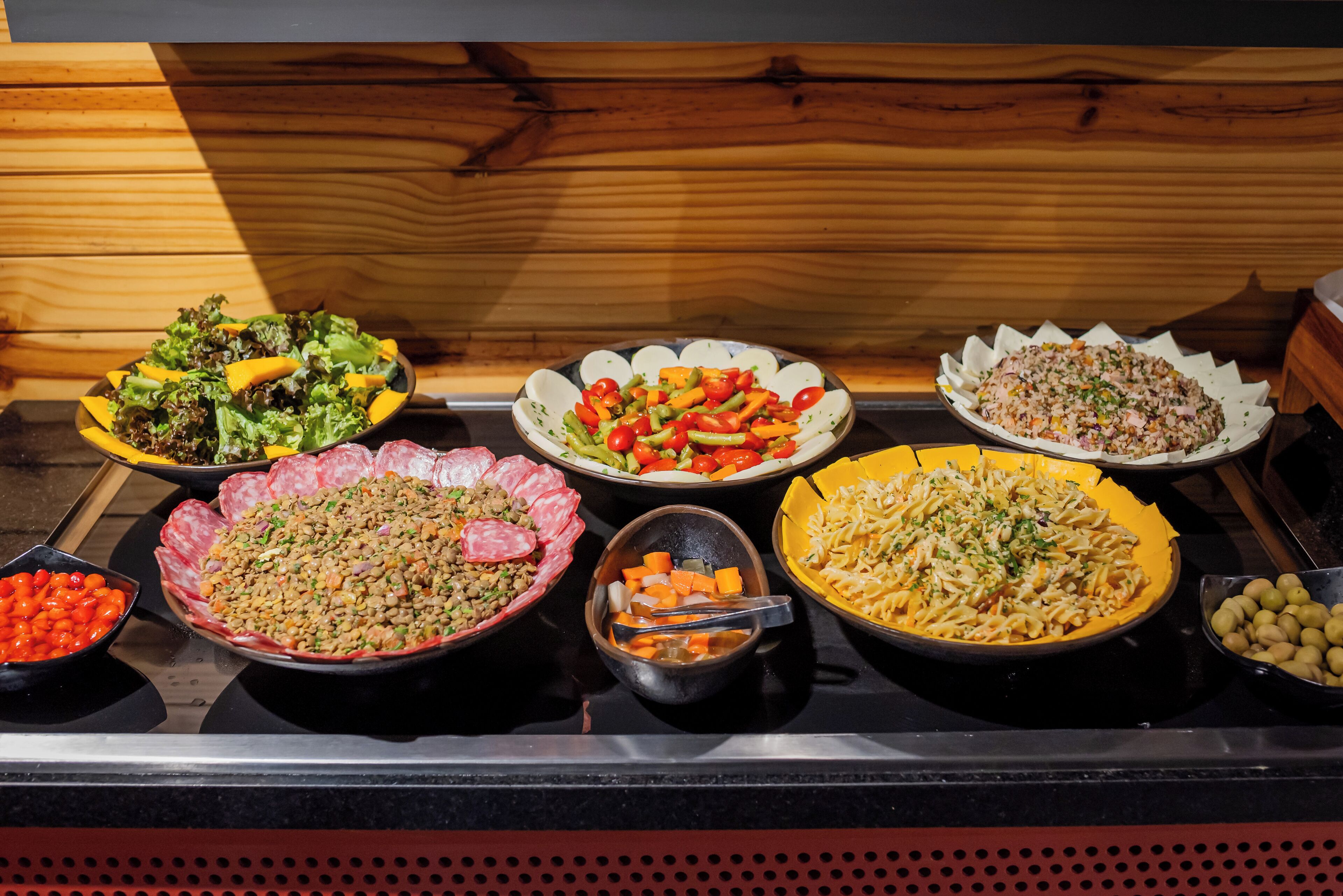 Un bufé con diversos platos, entre ellos ensaladas, pasta y un guiso de carne.