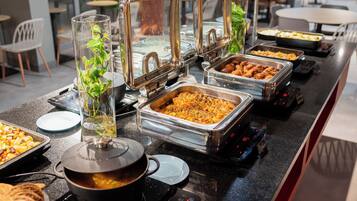 A buffet setup with various food items and a pot on an induction cooktop.