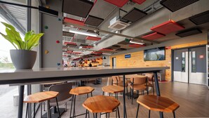 Un área de bar moderna con taburetes de madera, una planta grande en maceta y vistas al espacio de asientos exteriores.