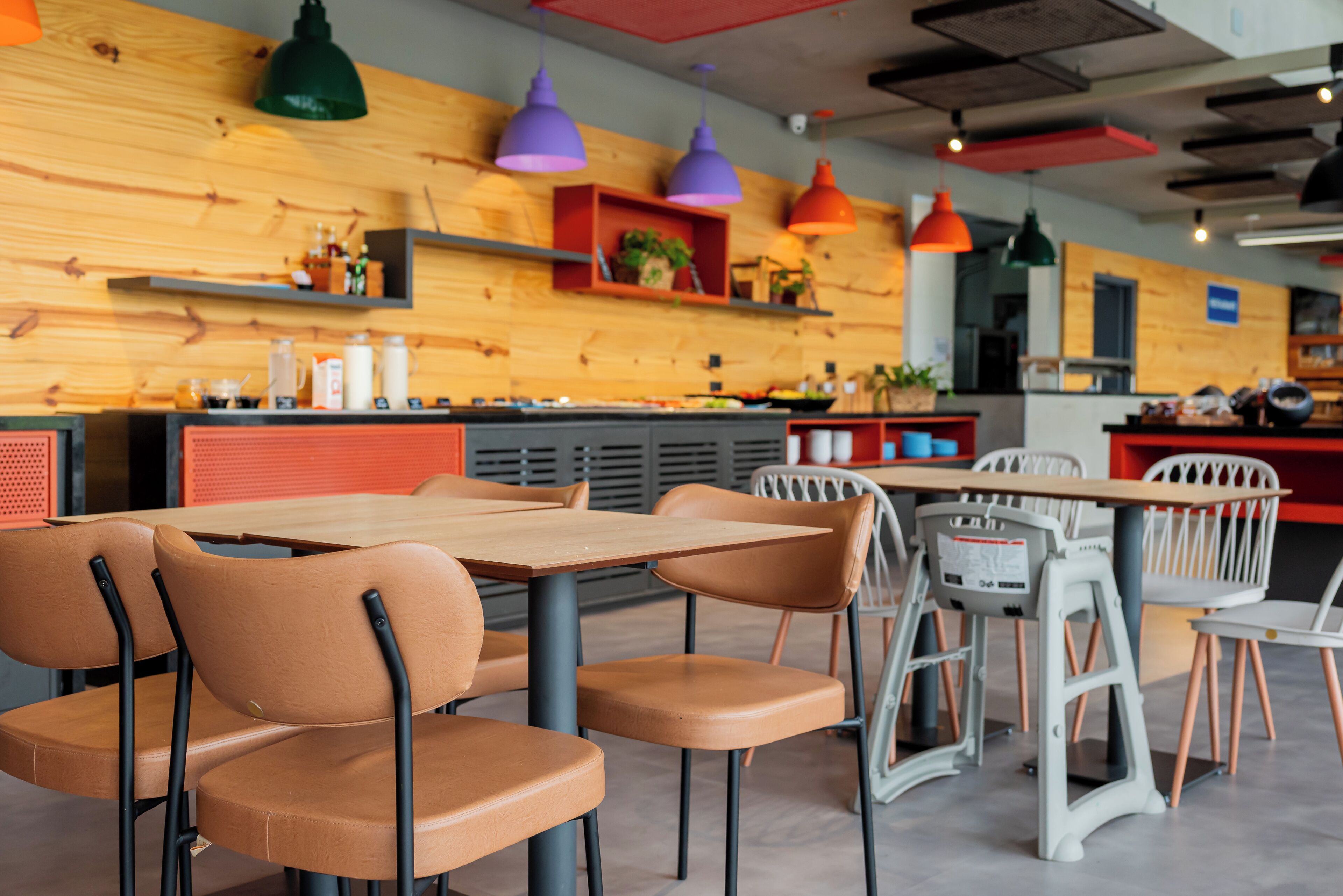 A modern restaurant interior with wooden walls, multiple tables and chairs, and pendant lighting.
