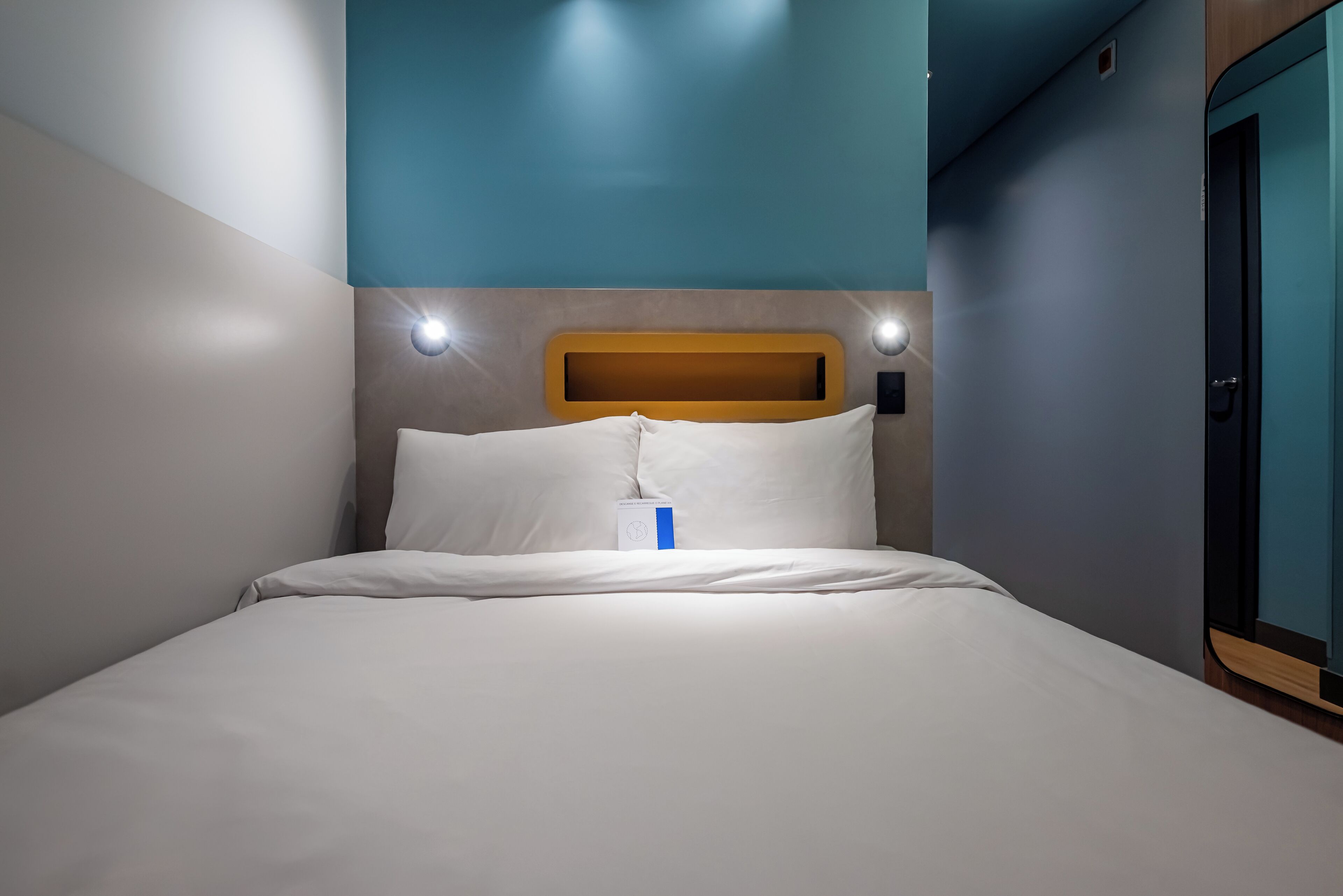 A hotel room with a bed, a wooden headboard, and a blue accent wall.