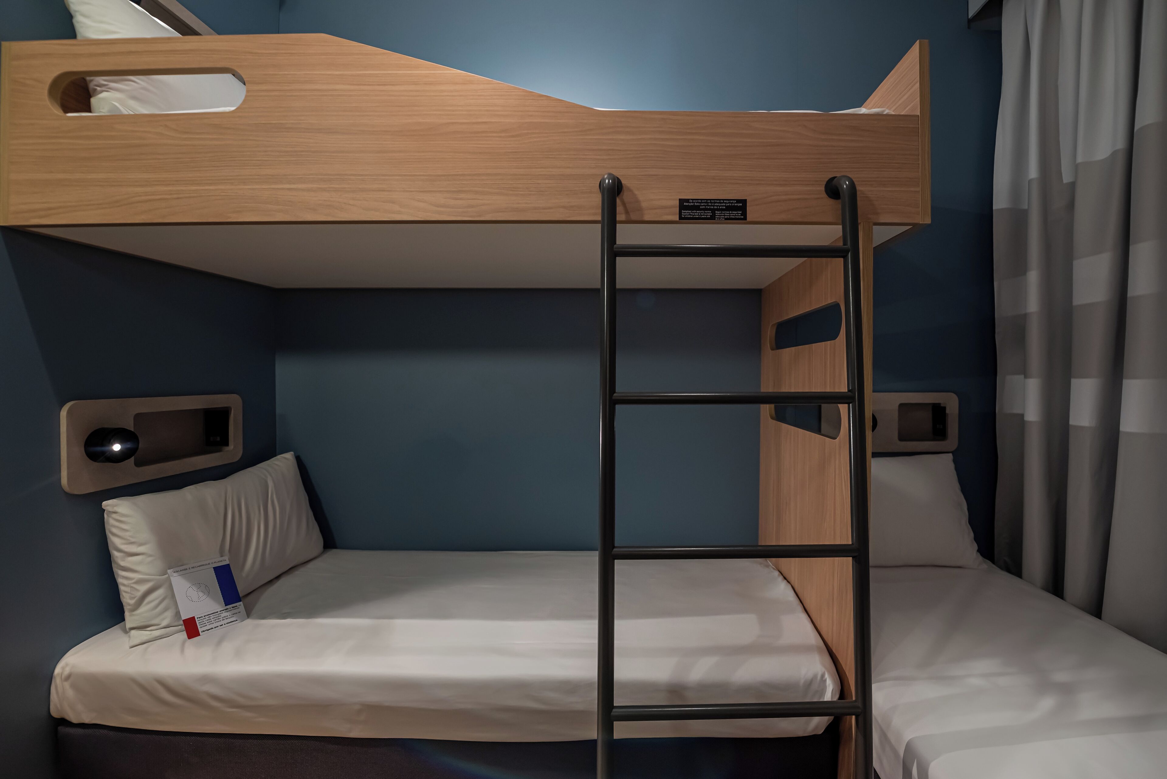 A bunk bed with a ladder, a bedside table with a lamp, and a pillow with a tag.