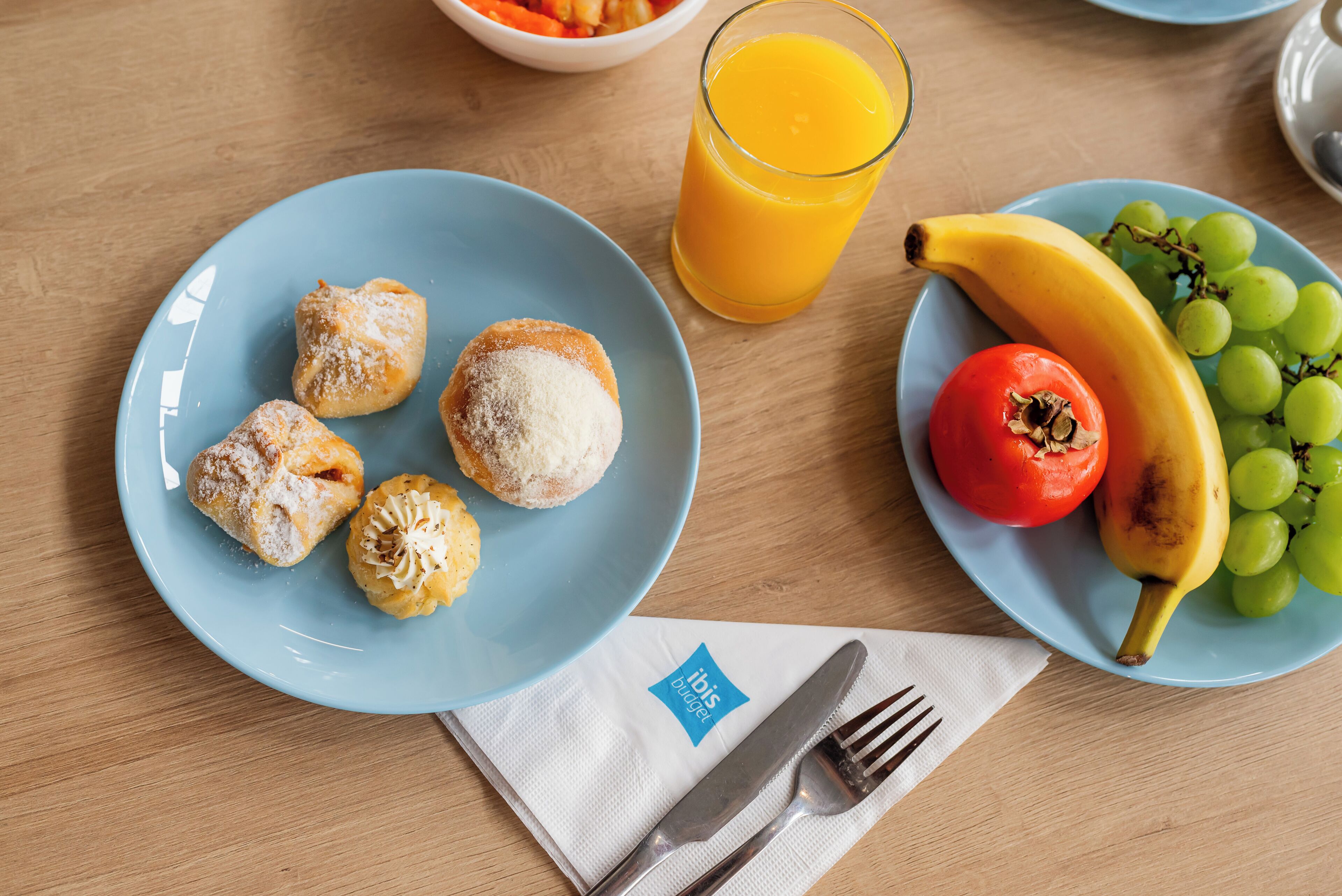 A table with a plate of pastries, a glass of orange juice, a banana, grapes, and a tomato.