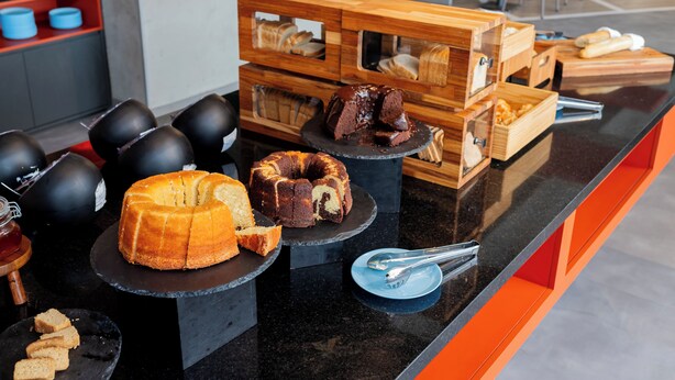 Un mostrador con diversas opciones de panadería, incluyendo pasteles y pan, expuestas sobre platos negros y cajas de madera.