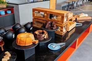 Un mostrador con diversas opciones de panadería, incluyendo pasteles y pan, expuestas sobre platos negros y cajas de madera.