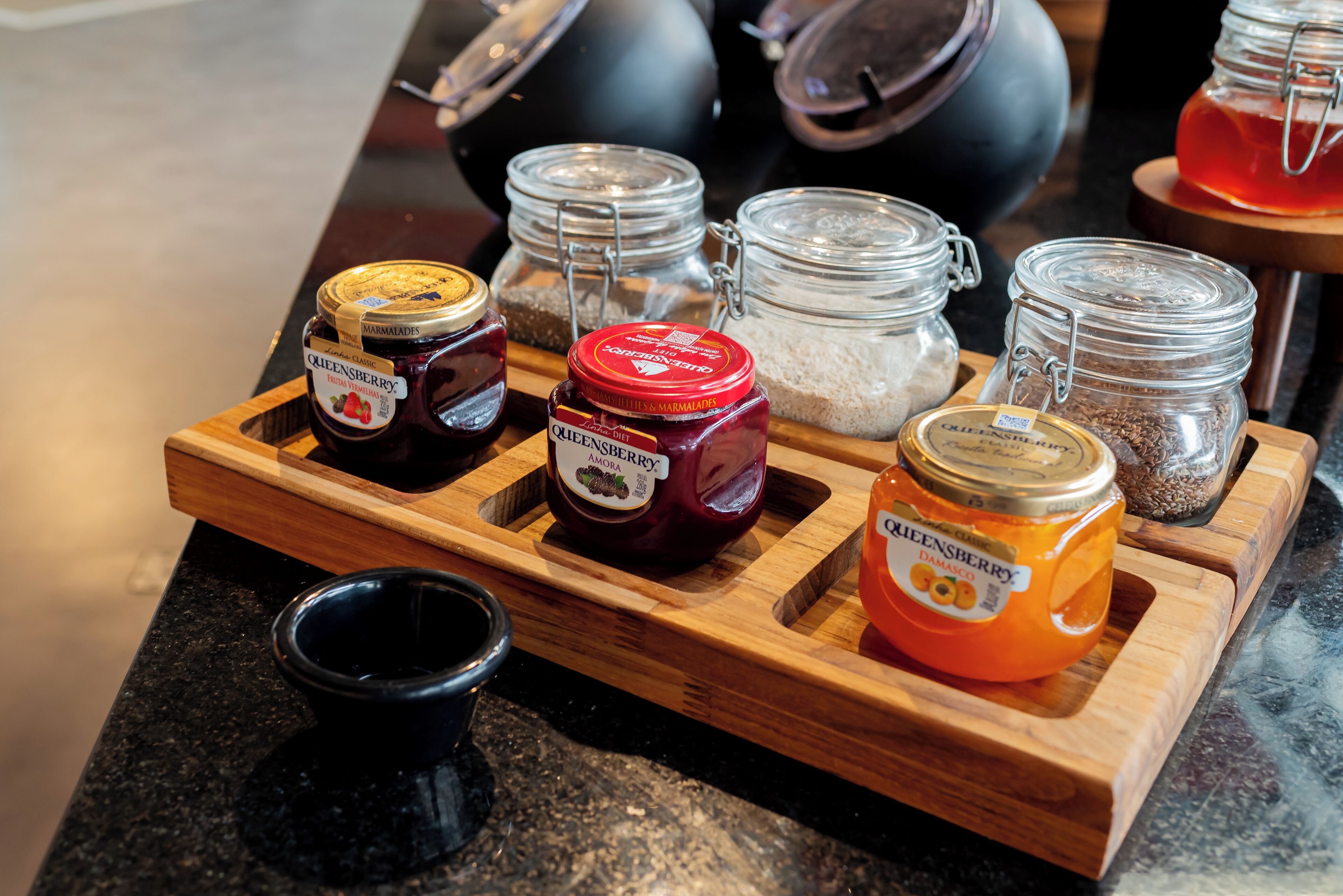 A wooden tray with various jars of preserves and spices on a kitchen counter.