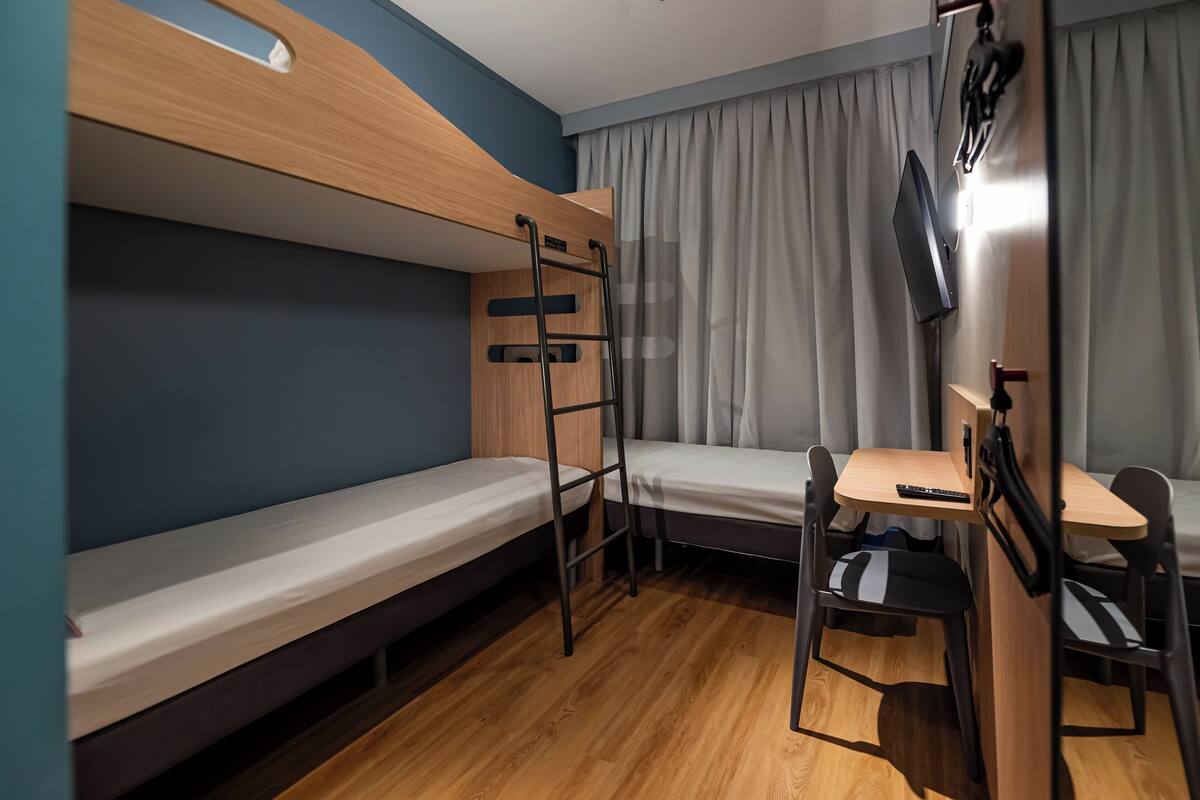Habitación con literas, escritorio, silla, televisor montado en la pared y ventana con cortinas.