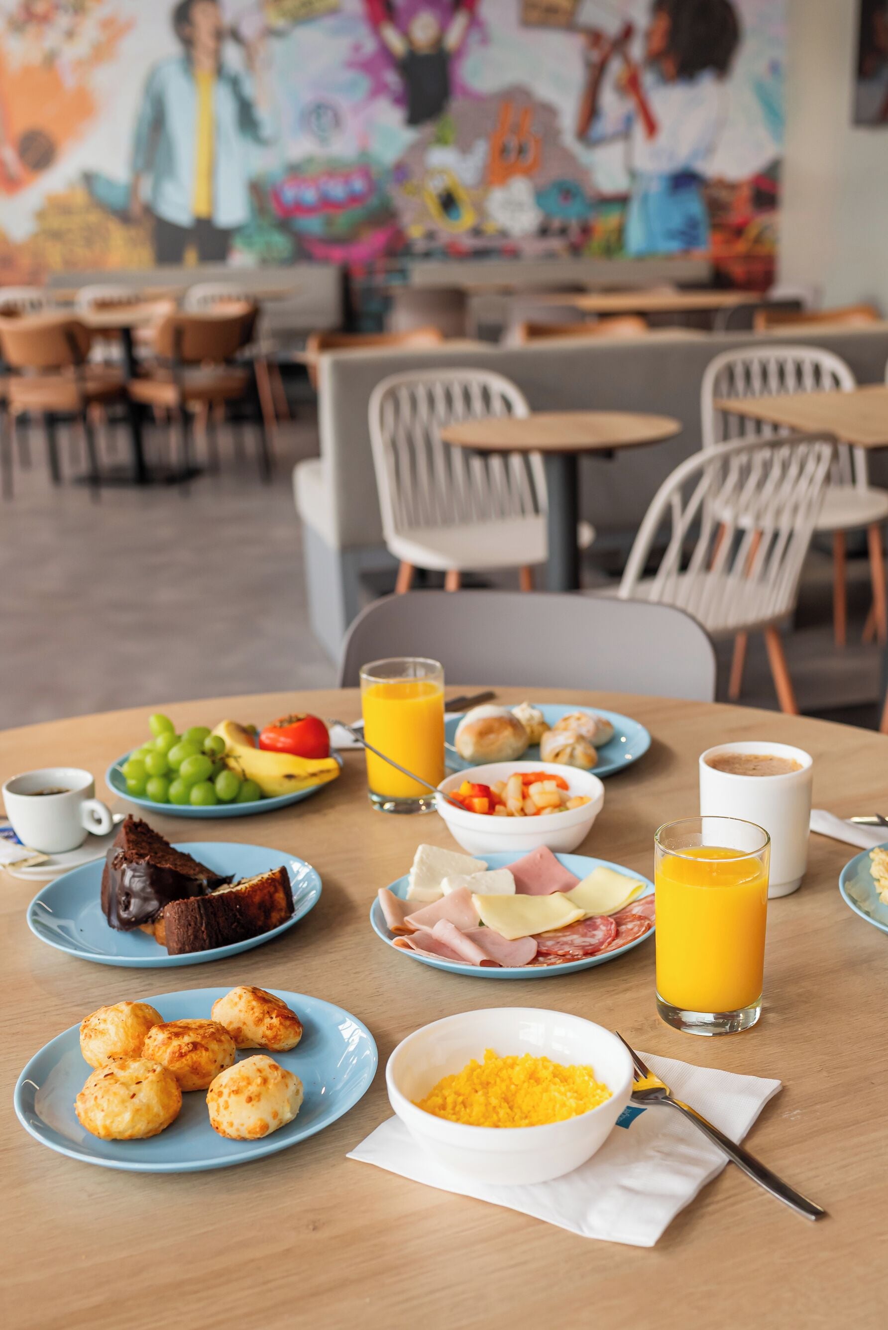 A breakfast table with plates of food, a bowl of cereal, and glasses of orange juice.