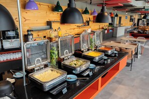 Zona de buffet con diversas estaciones de comida, que incluyen una barra de ensaladas y una estación de quesos, en un restaurante moderno.