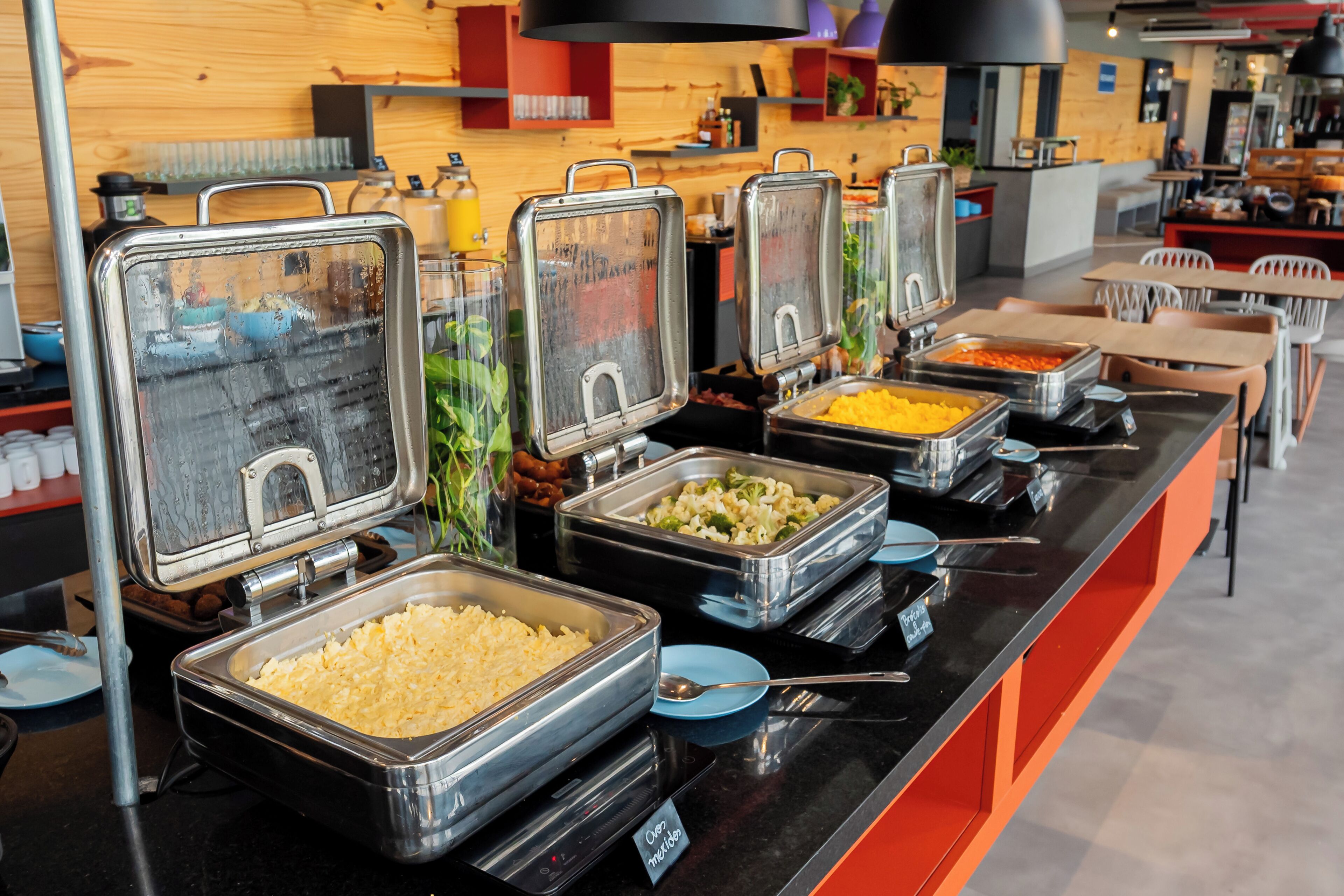 A buffet with various food options, including a large container of macaroni and cheese, a container of vegetables, and a container of scrambled eggs.