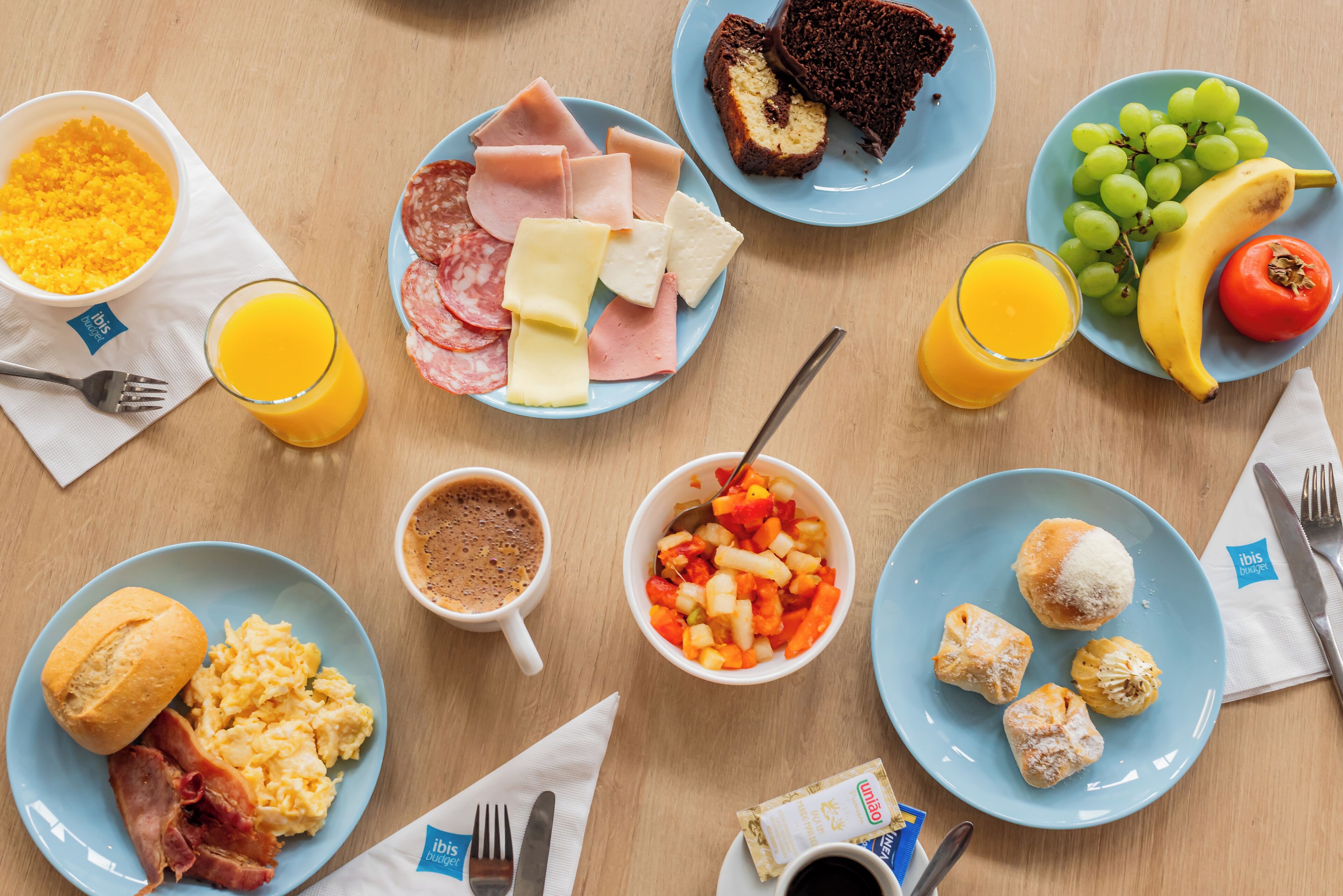 A breakfast table with plates of eggs, ham, cheese, toast, and fruit.