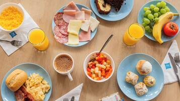A breakfast table with plates of eggs, ham, cheese, toast, and fruit.