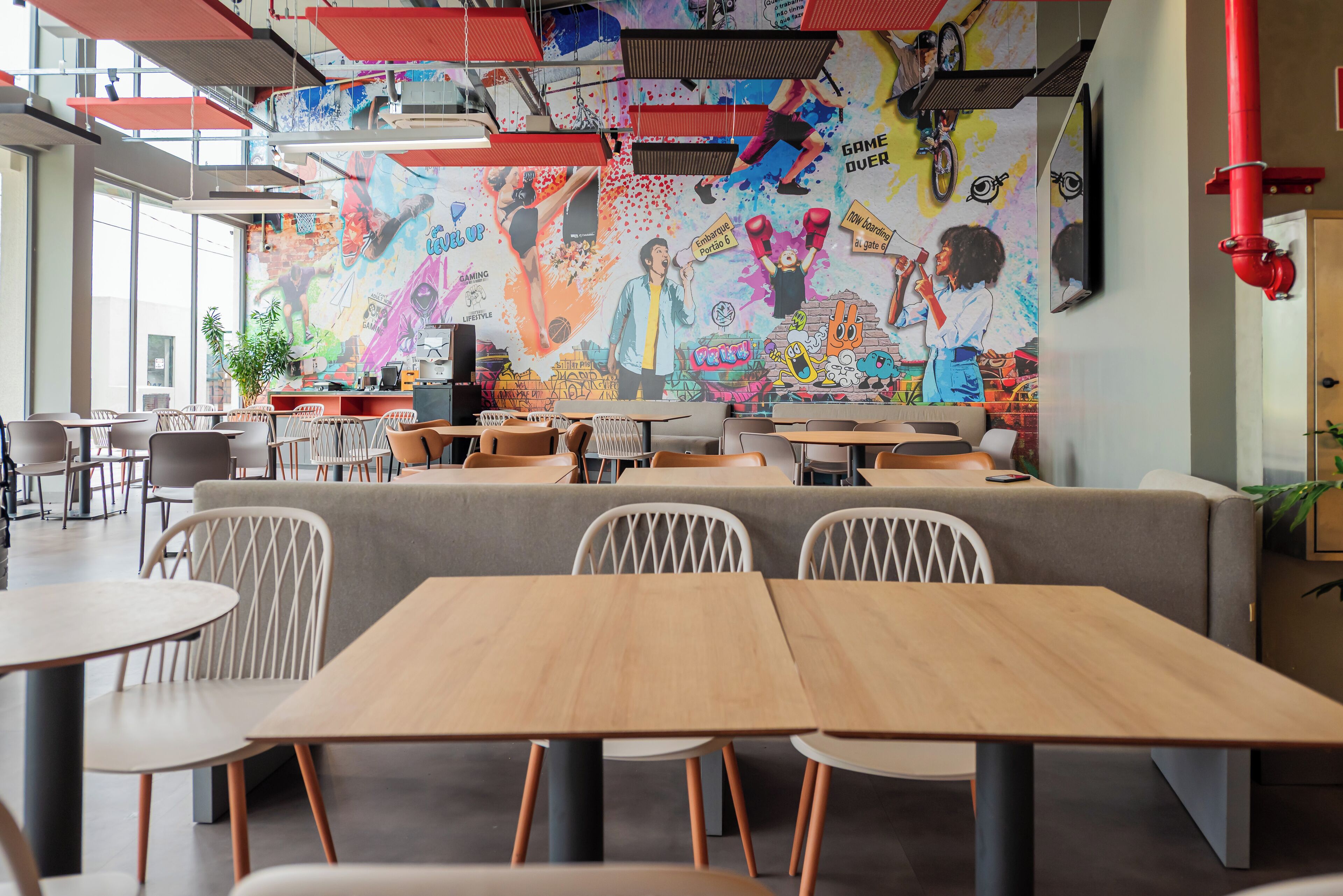 En moderne café med et farverigt muralmaleri, træborde og behagelige siddepladser.