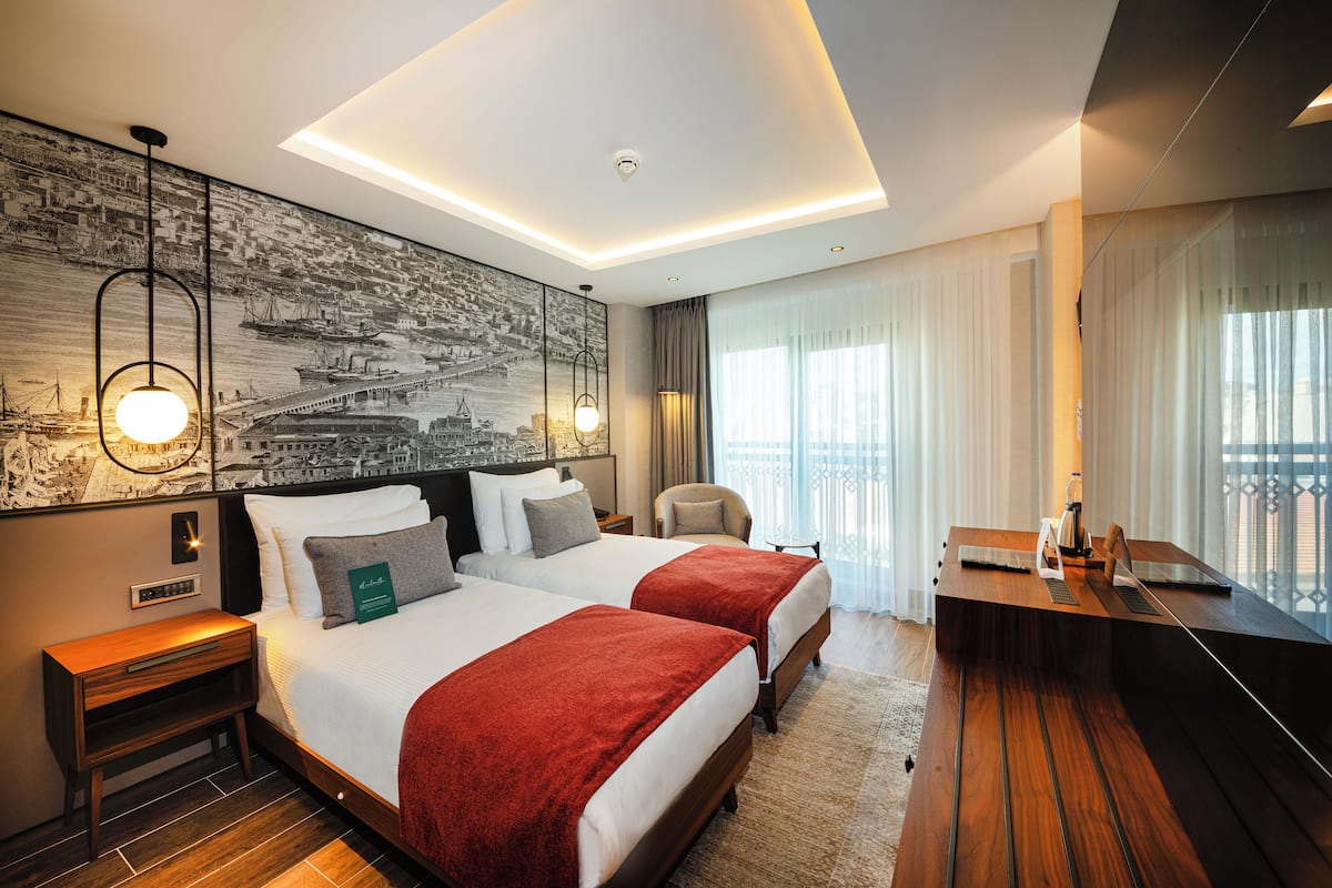 A hotel room with two beds, a desk, and a large window with curtains.