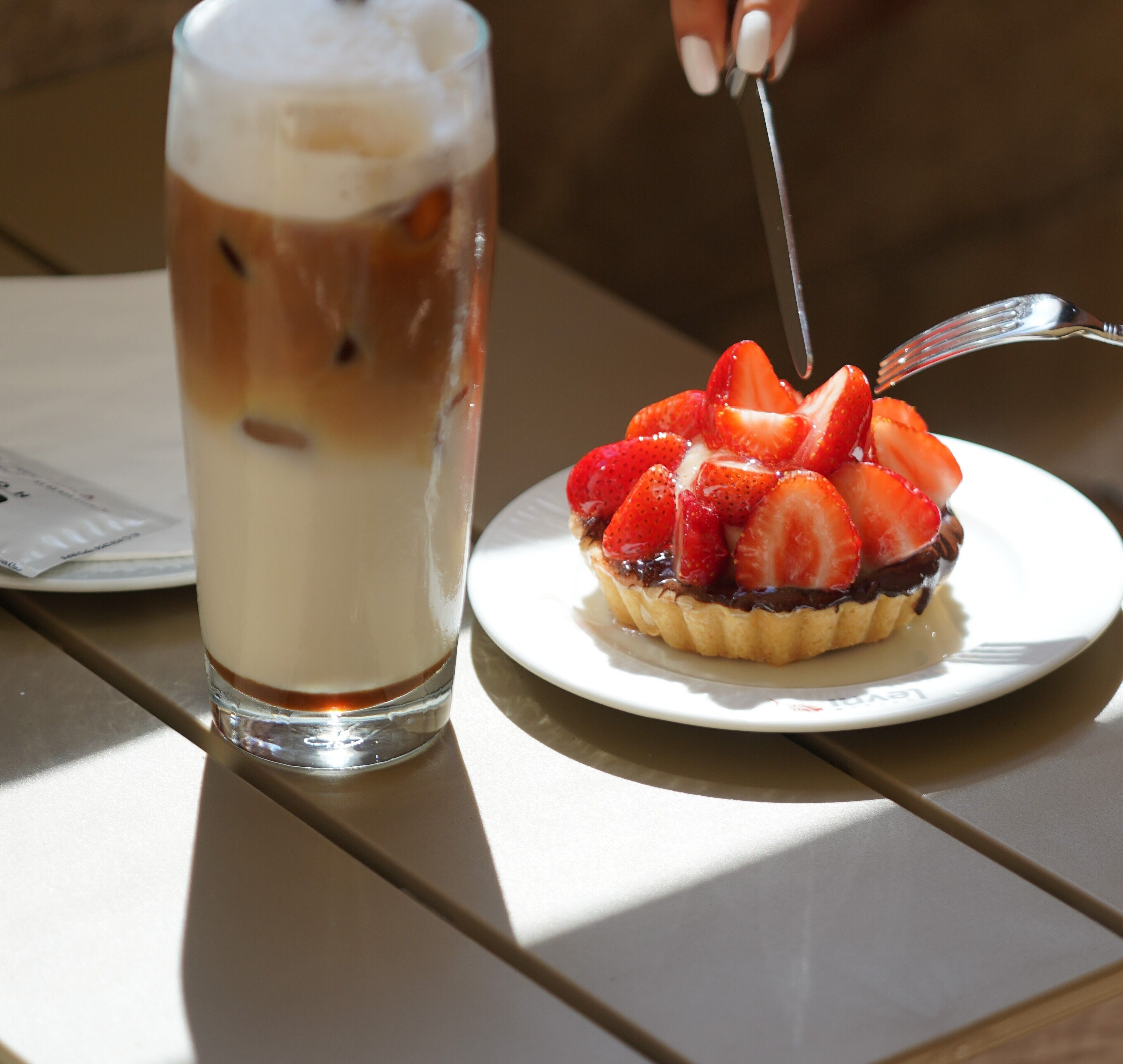 A dessert with strawberries and a glass of iced coffee on a table.