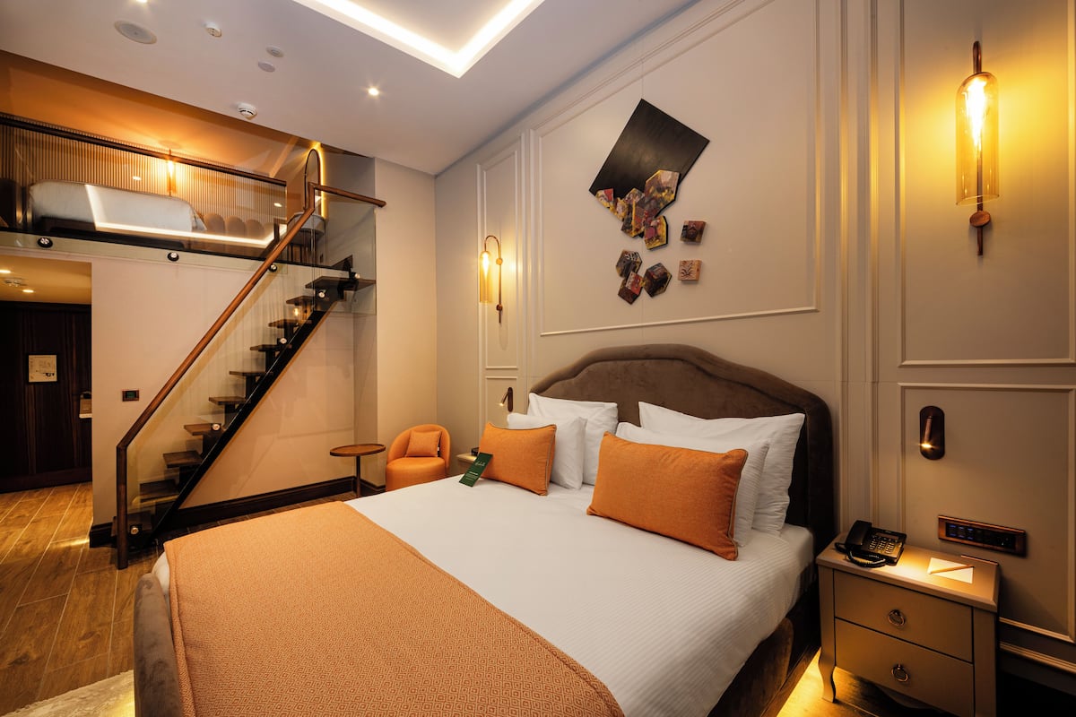 A hotel room with a large bed, a wooden staircase, a nightstand, and a wall-mounted light fixture.
