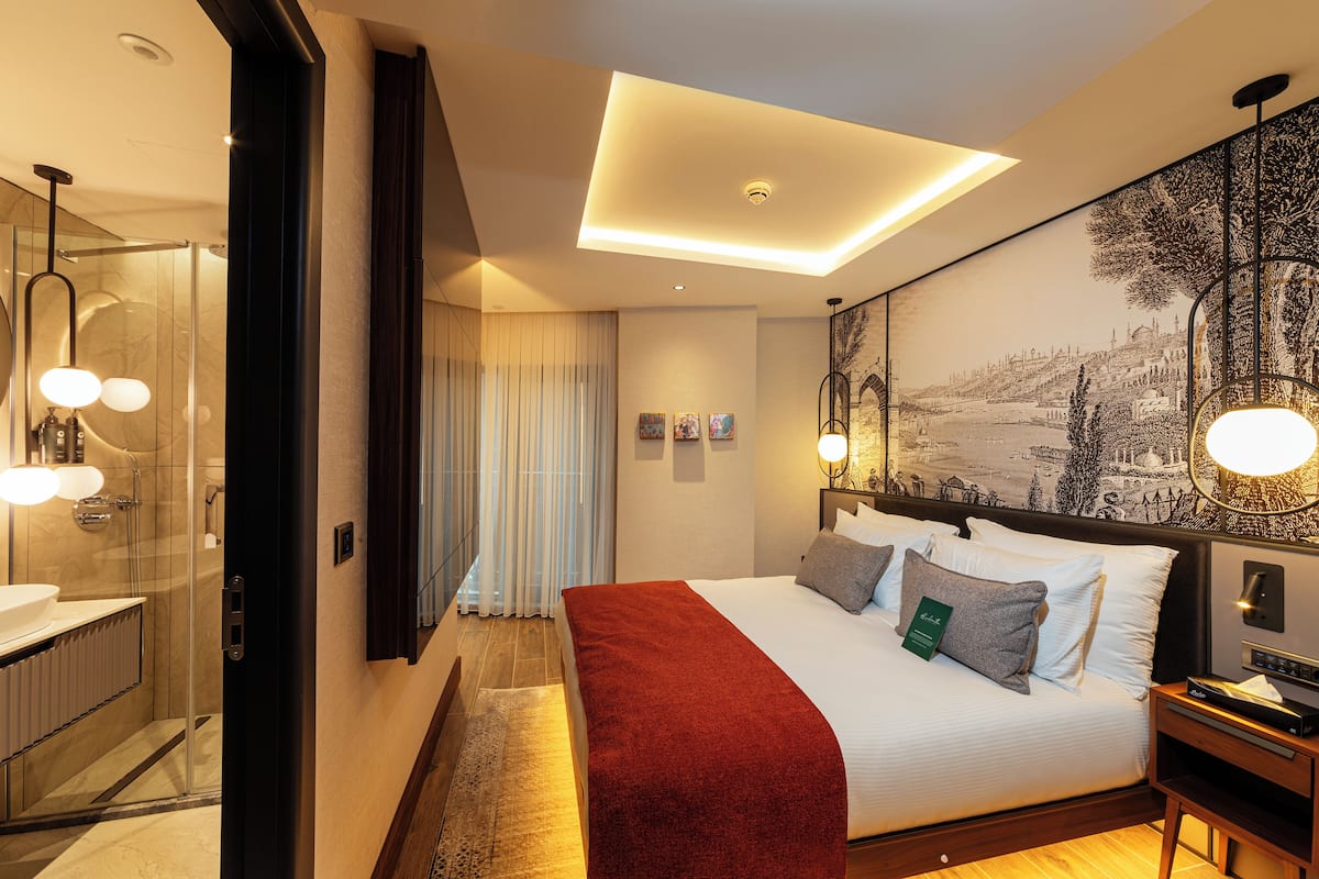 A modern hotel room with a large bed, a bathroom with a glass shower, and a mural on the wall.