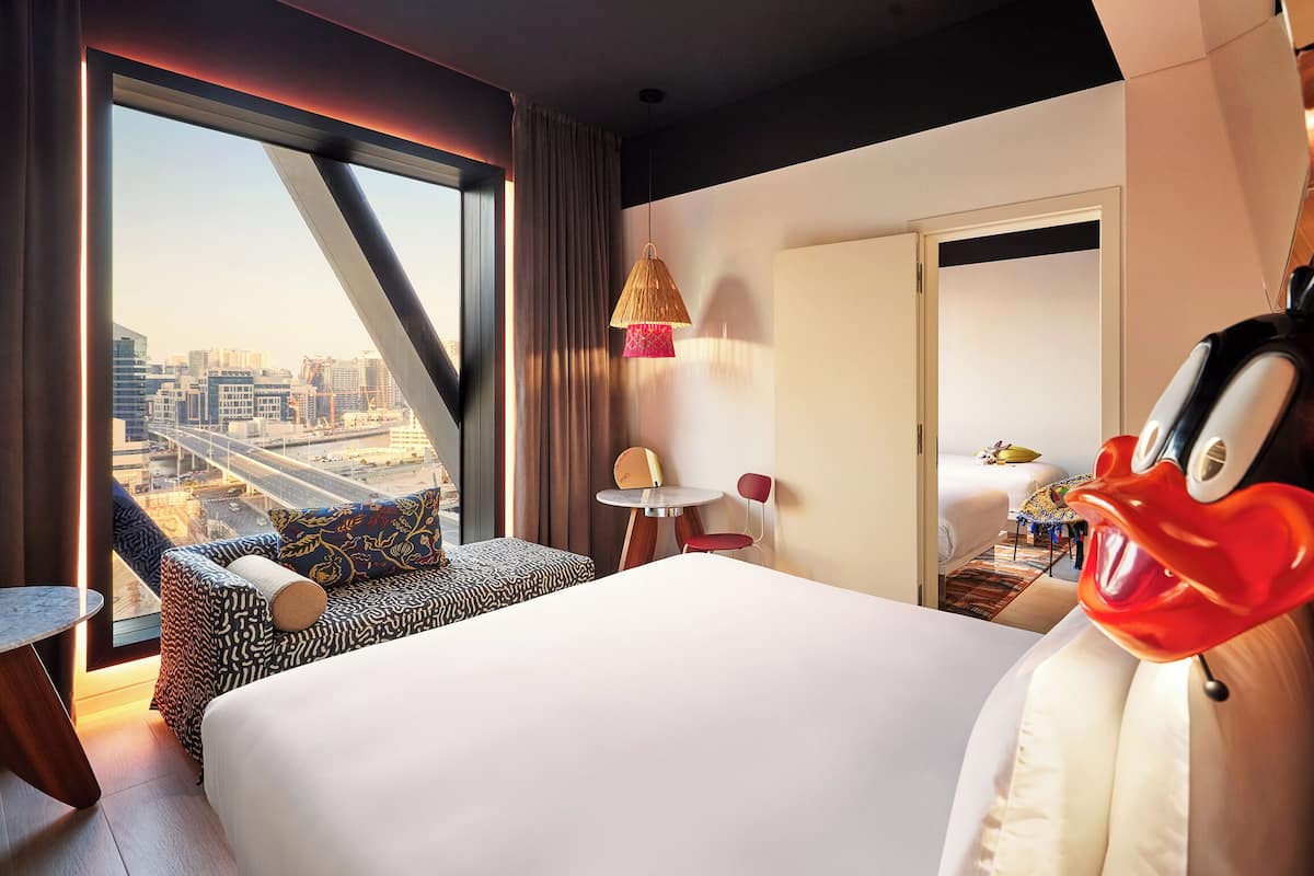 Une chambre d’hôtel avec un grand lit, une petite table, une chaise, une lampe et une vue sur le paysage urbain.