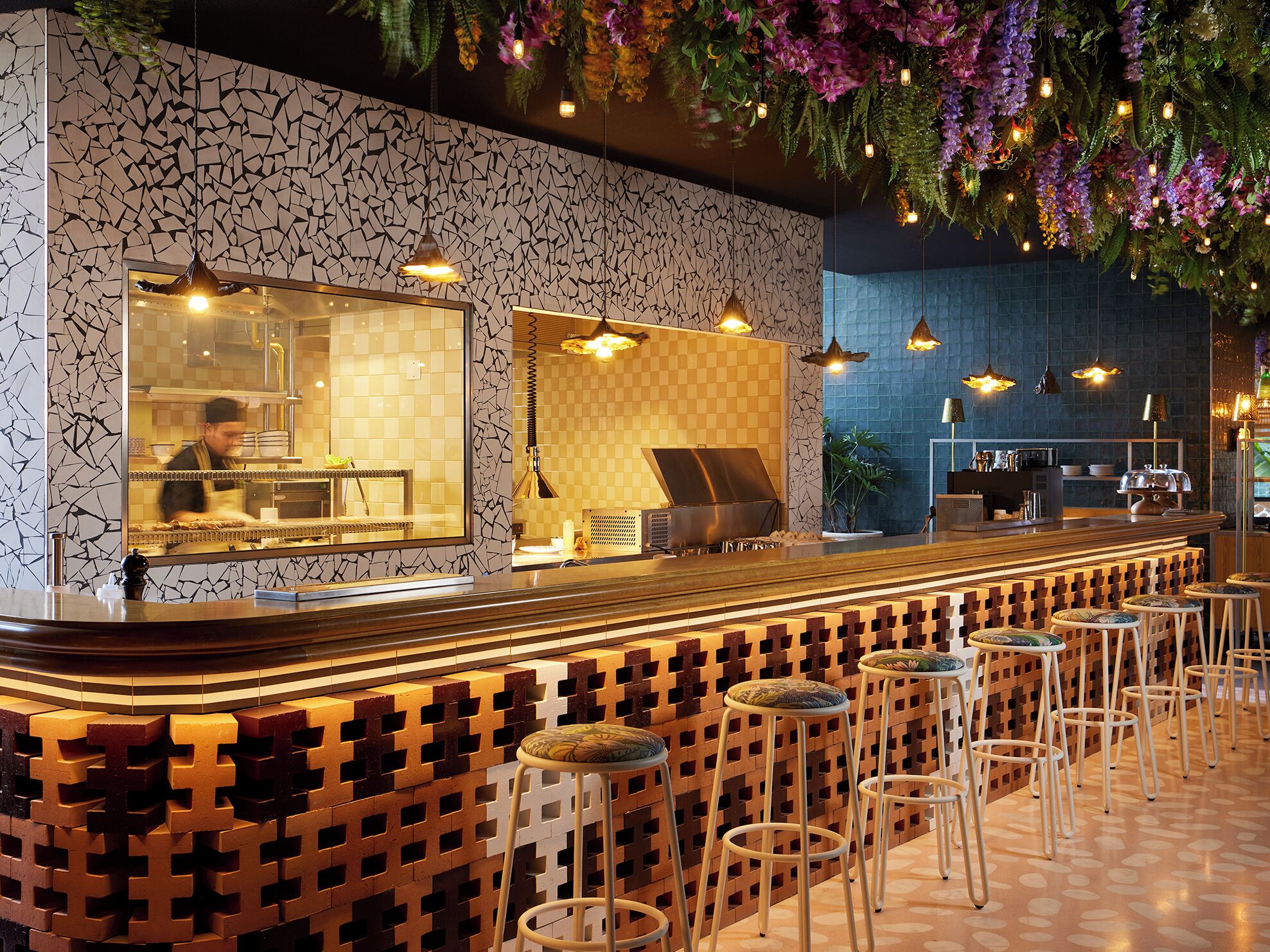 Uma área de bar com balcão, banquetas e luminárias pendentes.