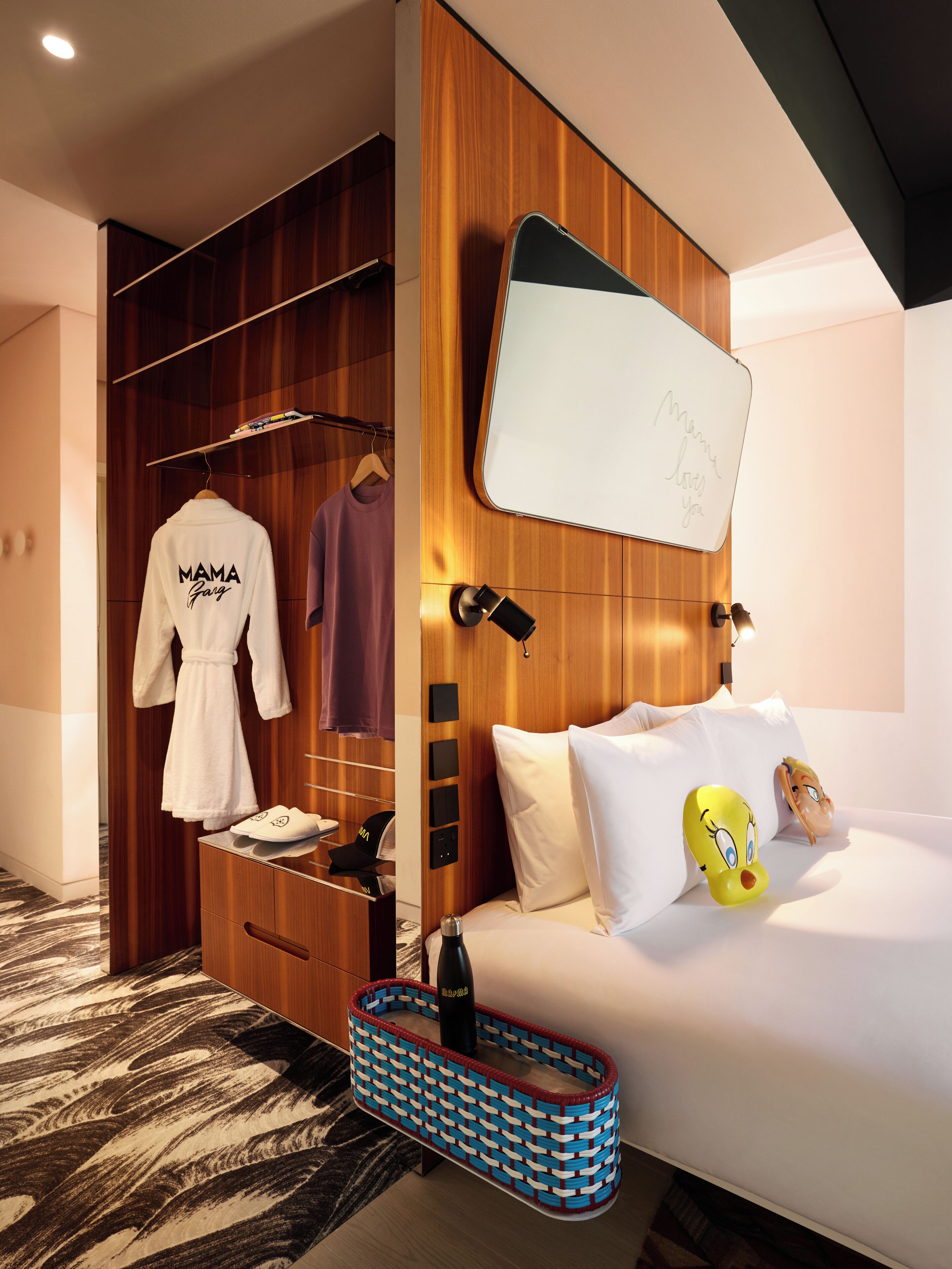 Ein Hotelzimmer mit einem Holzkleiderschrank, einem weißen Bademantel, einem Bett mit weißer Bettwäsche und einem Mickey Mouse Kissen.