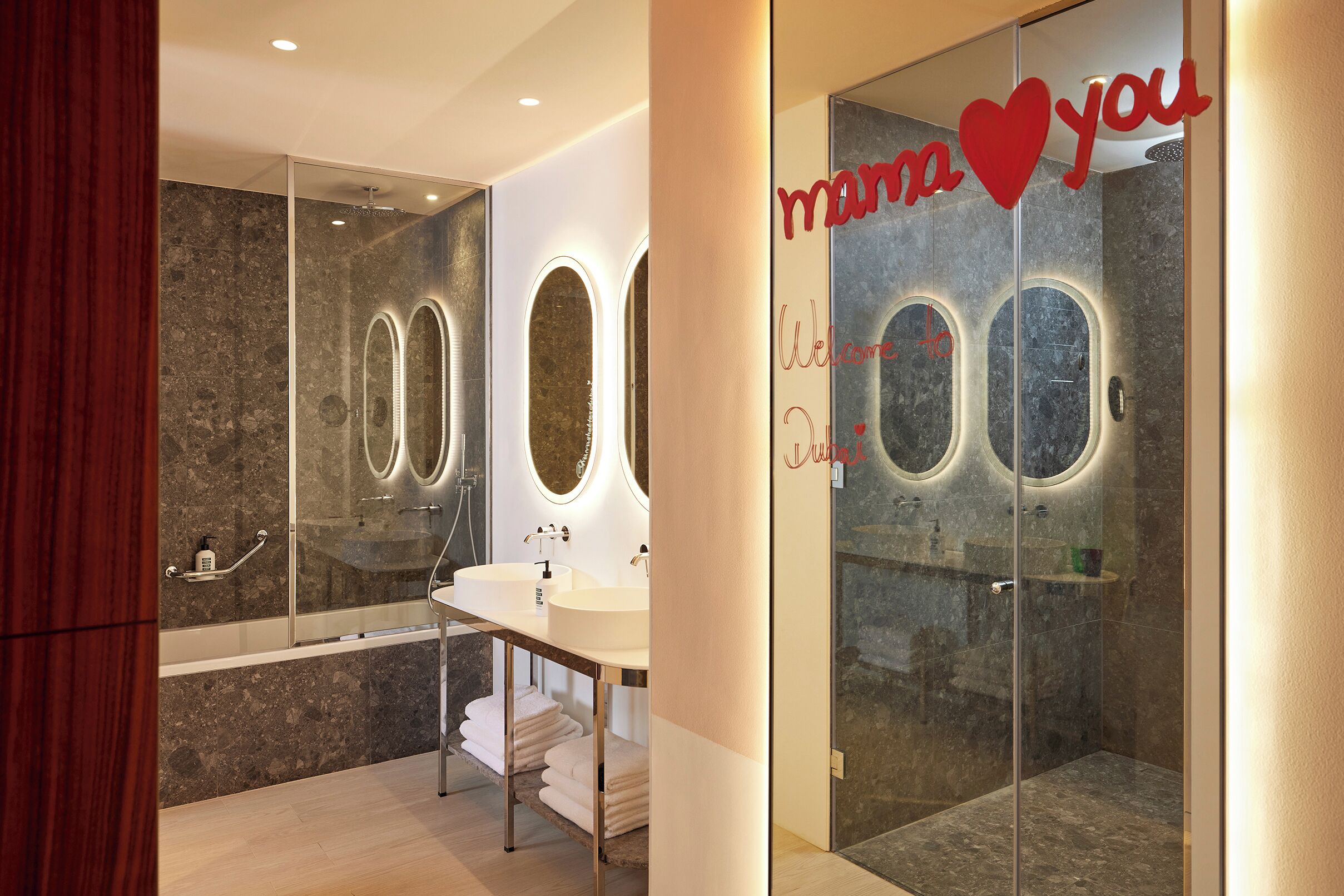 A modern bathroom with a glass shower enclosure, a vanity with a double sink, and a mirror with circular lights.