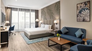 A modern hotel room with a large bed, a sofa, a desk with a chair, and a coffee table. - Mercure Riyadh Al Anoud (Riyadh)