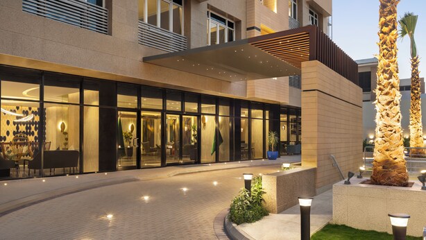 A modern hotel entrance with glass doors, a covered outdoor seating area, and a well-lit pathway. - Mercure Riyadh Al Anoud (Riyadh)