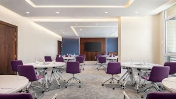 A conference room with round tables, purple chairs, and a large screen at the front.