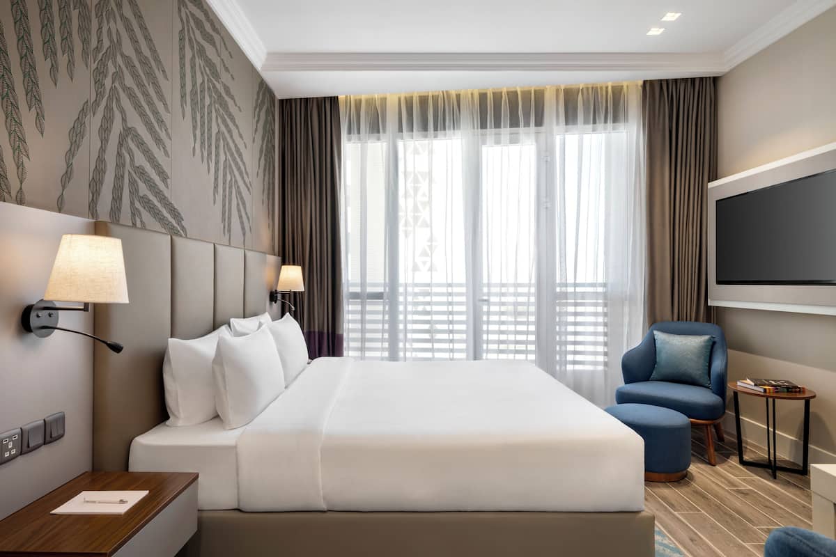 A hotel room with a large bed, two bedside lamps, a TV, a chair, and a small table.