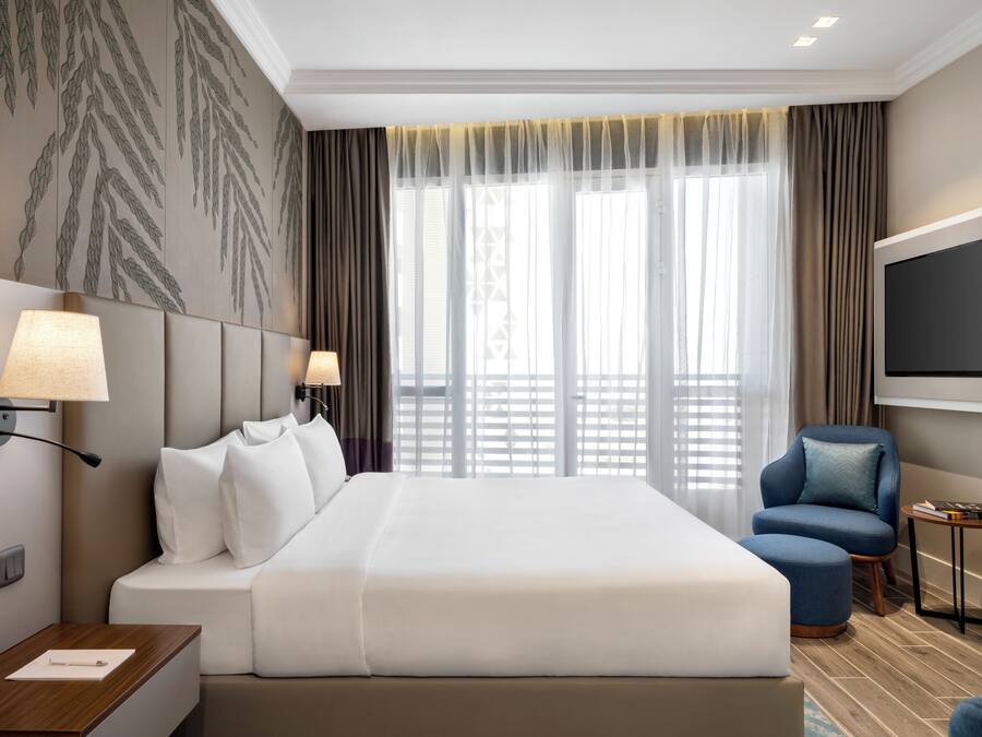 Una habitación de hotel con una cama grande, dos lámparas de noche, un televisor, una silla y una mesita.