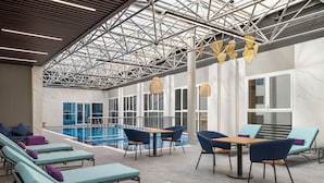 A modern indoor pool area with lounge chairs, tables, and a clear view of the pool. - Mercure Riyadh Al Anoud (Riyadh)