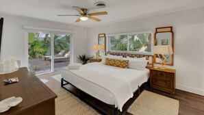 A bedroom with a bed, a desk, a nightstand, a ceiling fan, and a view of the outdoors. - Towering Palms in Wilton Manors (Wilton Manors)