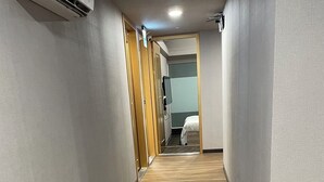 Een hotelgang met houten vloer, een bed op de achtergrond en een airconditioning aan de muur.