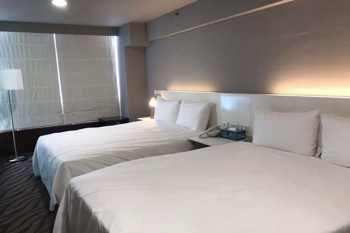 A hotel room with two beds, a bedside table with a lamp, a phone, and a small blue box.