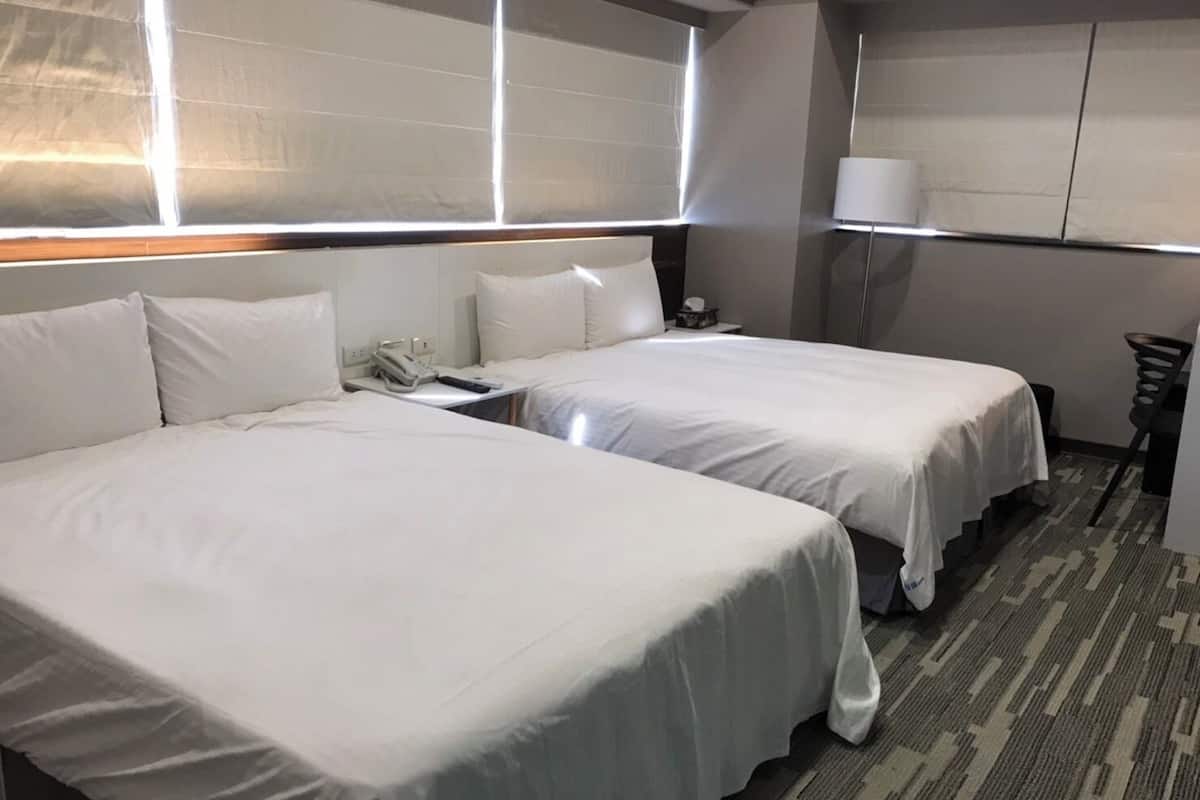 A hotel room with two beds, a nightstand, a lamp, and a chair.