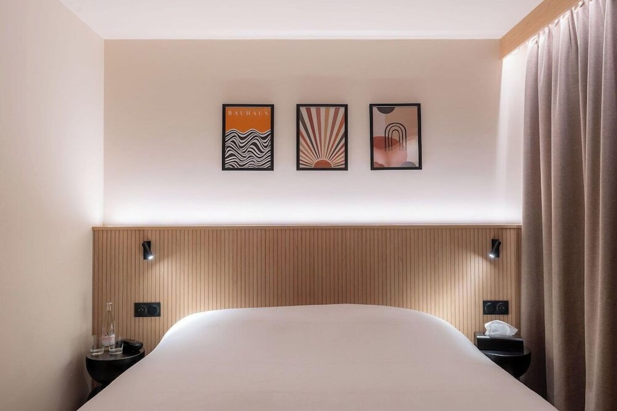 Een hotelkamer met een groot bed, twee nachtkastjes, een houten hoofdbord en drie ingelijste kunstwerken aan de muur.