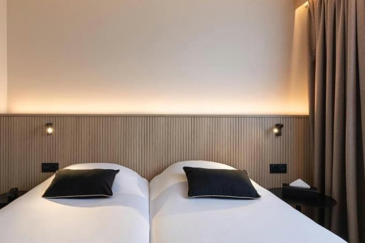 Een tweepersoonsbed met hoofdeinde, twee nachtkastjes en een wandlamp.
