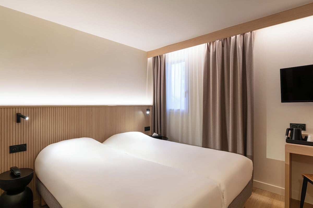 Een hotelkamer met een groot bed, een flatscreen televisie, een bureau met koffiezetapparaat en een raam met gordijnen.