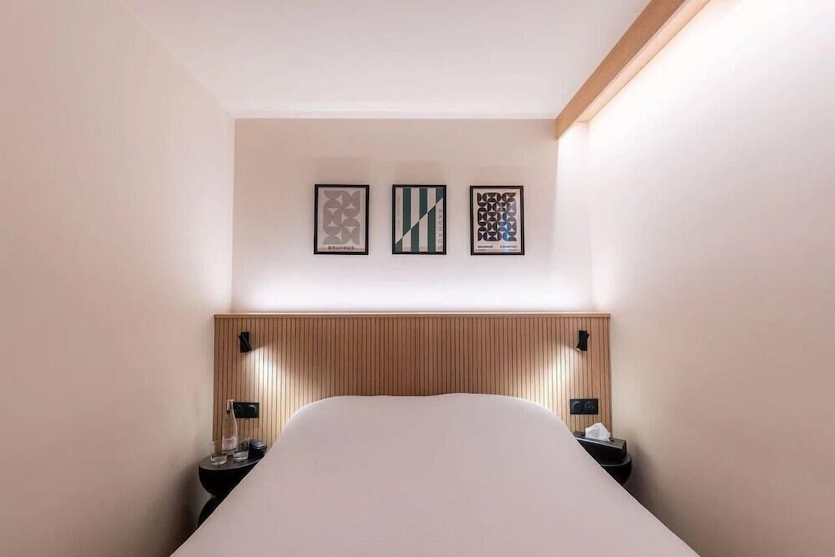 Een hotelkamer met een bed, nachtkastjes, een houten hoofdbord en drie ingelijste kunstwerken aan de muur.