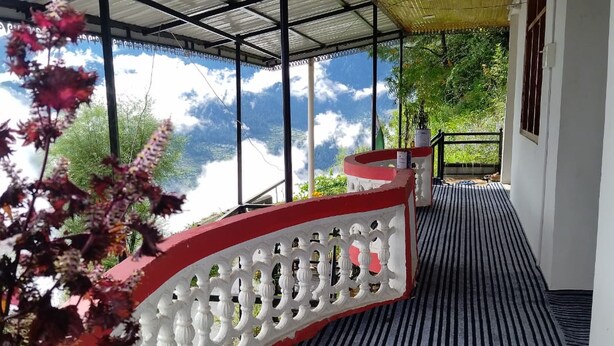 A covered balcony with a view of a mountainous landscape, a red and white railing, and a striped floor. - Fresh View Homestay (Sainj)